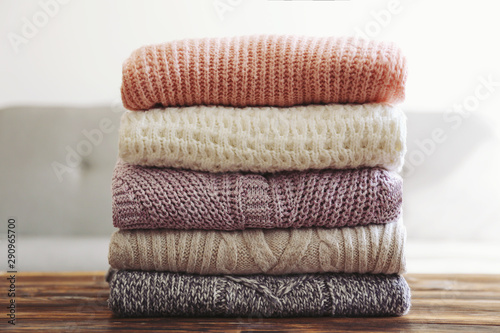 Bunch of knitted pastel color sweaters with different knitting patterns perfectly folded in stack on brown wooden table, white brick wall background. Fall winter season knitwear. Close up, copy space photo