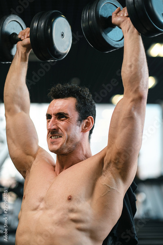 Foto Man bodybuilder lifting dumbbells working focused on his biceps at the gym