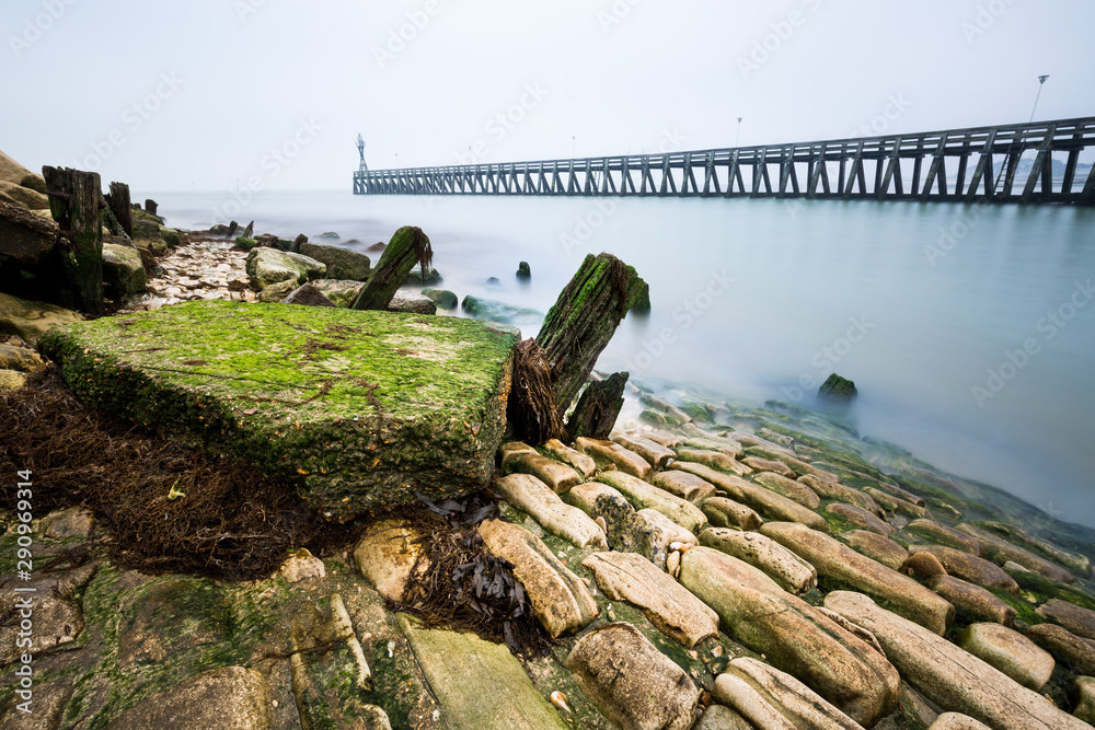 French landscape with a stone waterfront and a distant wooden pier covered by haze