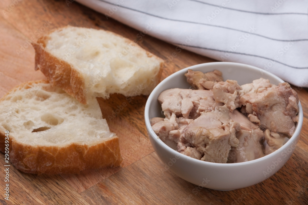 Canned cod liver in a bowl with two slices of ciabatta on a wooden board
