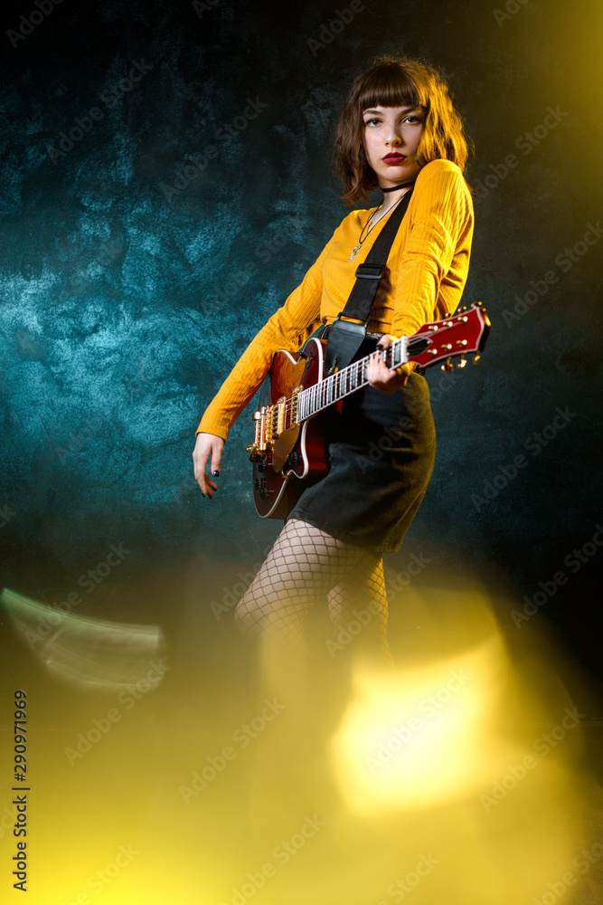Portrait of beautiful young hipster woman with curly hair with red guitar in neon lights. Rock musician is playing electrical guitar. 90s style concept.