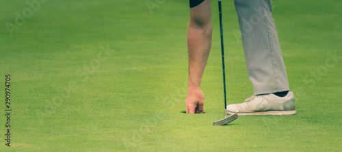 Golfer is taking the ball out of the hole.
