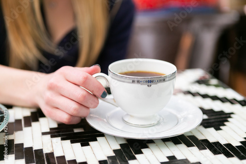 Girl holding cup of coffee in antique cup at cafe, close up, copy space