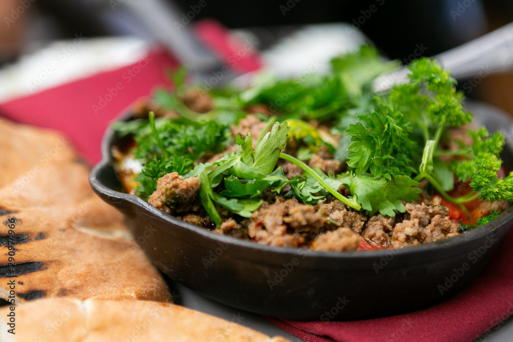 Shakshuka with sausage, tomatoes, egg, parsley, in cast iron skillet with pita bread