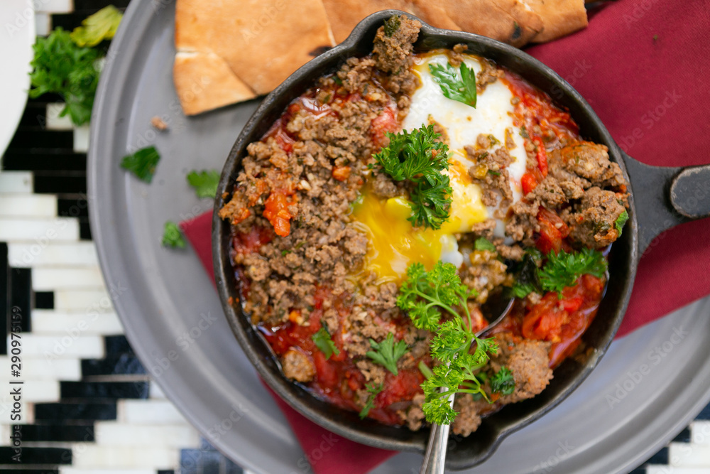 Shakshuka with sausage, tomatoes, egg, parsley, in cast iron skillet with pita bread Shakshuka with sausage, tomatoes, egg, parsley, in cast iron skillet with pita bread