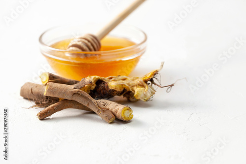 Raw root plant Rumex crispus (yellow dock) and honey on white concrete background
