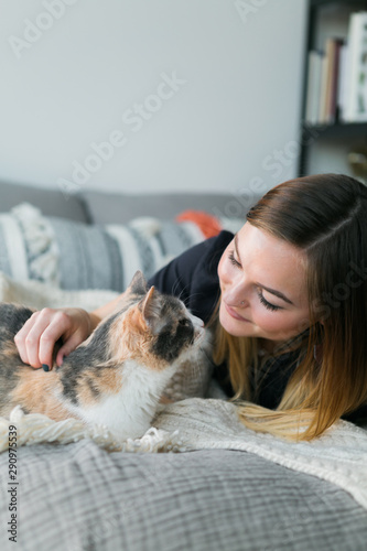 Cute girl cuddling with calico cat on bed in apartment, copy space, sweet