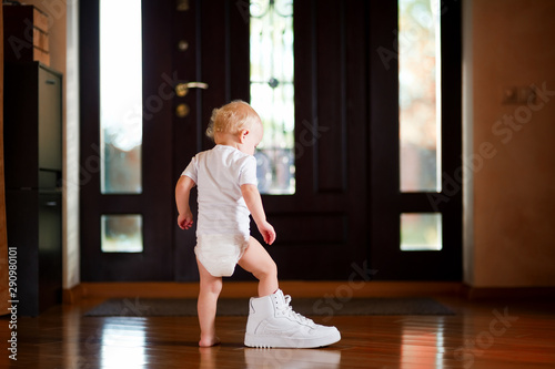 фотографія baby girl puts on a white dad's sneaker