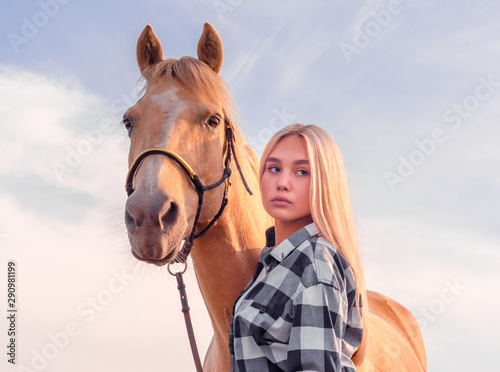 portrait of a young girl blonde with a beige horse against a blue sky with white clouds