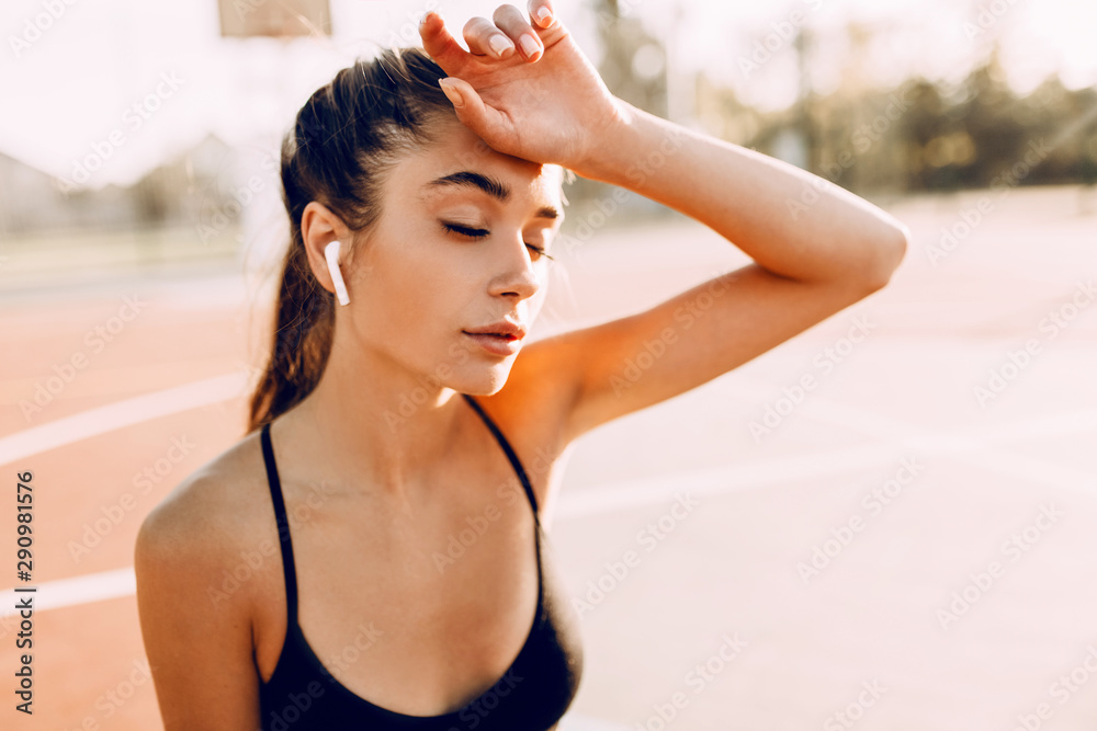Image of beautiful athletic woman outdoors in the morning, tired sportswoman listening to music with wireless headphones