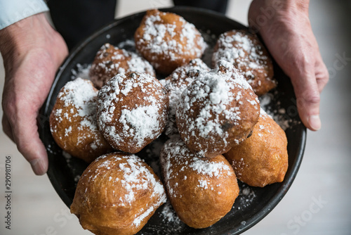 man showing oil dumplings (oliebollen) on black plate. Traditional treat on New Years Eve in The Netherlands