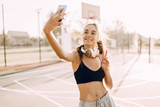 Happy fitness girl with headphones taking selfie outdoors while doing sports