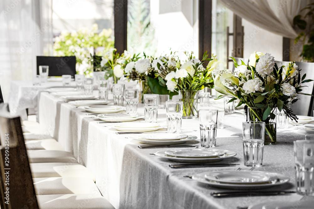 Beautiful table setting in a restaurant. White tablecloth, white cutlery, bouquets of flowers