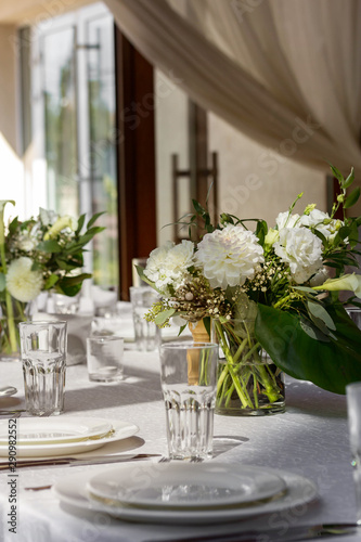 Beautiful table setting in a restaurant. White tablecloth, white cutlery, bouquets of flowers