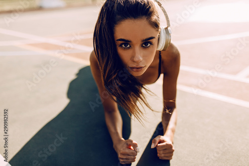 Closeup of a serious female athlete in the headphones makes the bar exercise in the open air
