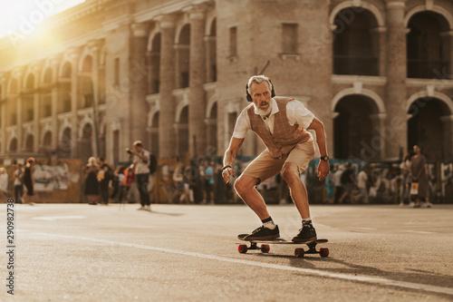 Stylish handsome man ride on skateboard on city street in sunset evening. Smiling modern male portrait. Skater enjoy urban lifestyle