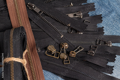 Pack a lot of black brown metal brass antique zippers stripes with sliders pattern for handmade sewing tailoring haberdashery leather craft on the blue wooden background