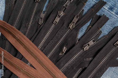 Pack a lot of black brown metal brass antique zippers stripes with sliders pattern for handmade sewing tailoring haberdashery leather craft on the blue denim background