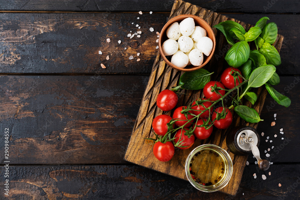 Fresh cherry tomatoes, basil leaves, mozzarella cheese and olive oil on old wooden background. Caprese salad ingredients. Selective focus.