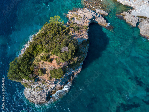Aerial view of Sveti Nicola, Budva island, Montenegro. Hawaii beach, umbrellas and bathers and crystal clear waters. Jagged coasts with sheer cliffs overlooking the transparent sea. Wild nature