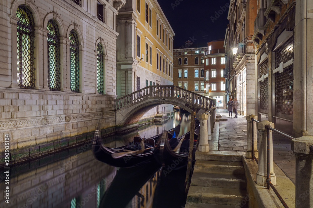 Narrow canal between colorful historic houses in Venice at night.
