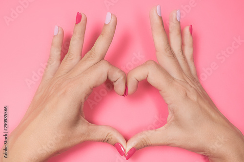 Closeup top view of beautiful female hands with modern trendy multicolor manicure isolated on pink background. Woman making heart gesture with 2 hands. Love and family concept.
