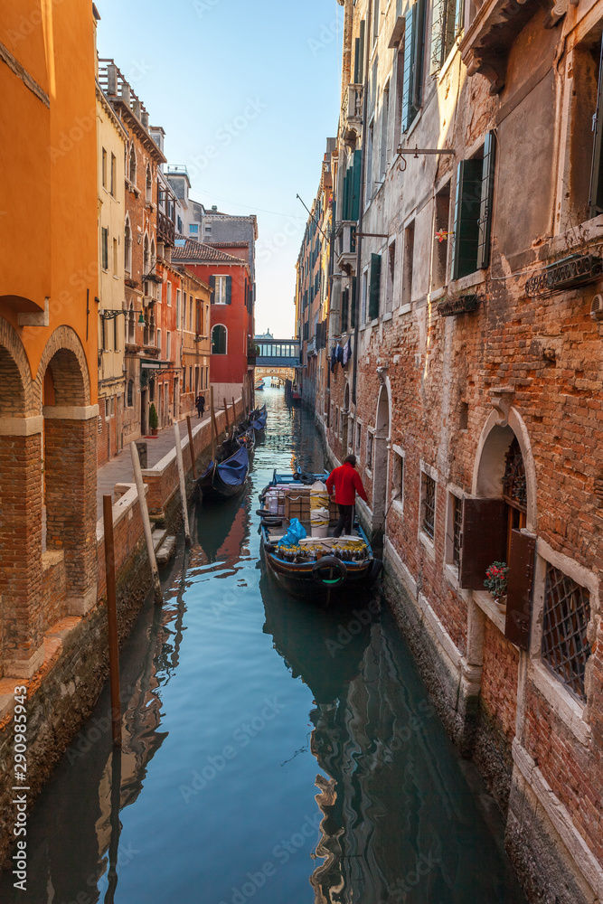 Boats on narrow canal between colorful historic houses in Venice.