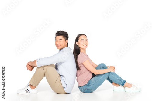 young asian couple sitting back to back and looking at camera on white background © LIGHTFIELD STUDIOS