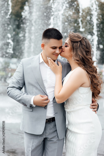 Young couple in love together in summer. Young lovers kissing during their romantic date. Cheerful couple hugging and kissing. Photo of an elegant woman in a white dress hugging her lover