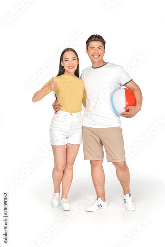 happy asian man holding beach ball and hugging girlfriend showing thumb up on white background