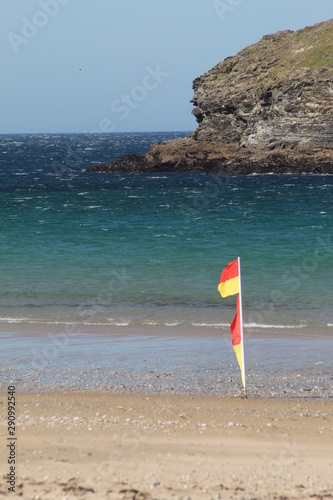 Gull rock, Portreath Beach, Cornwall in summer with Lifeguard swim flag in foreground