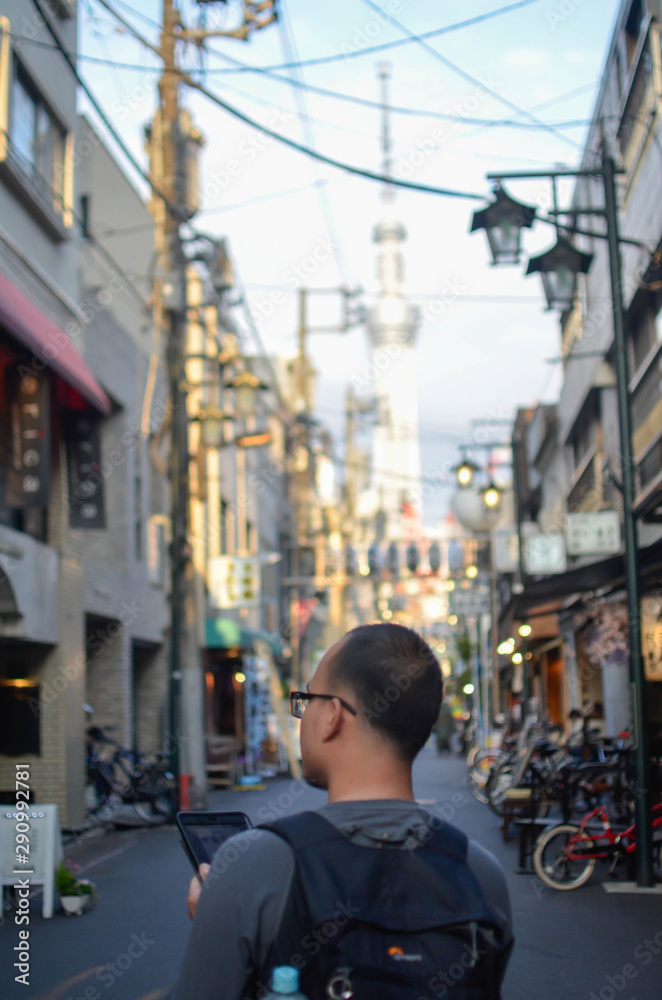 Fototapeta premium A man holding a tablet /mobile phone while using online map or searching the destination on internet and walking in the center city of Toyko in summer sunset time