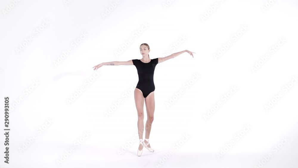 Ballerina in black suit practicing in ballet in light studio. Young girl isolated on white wall dancing classic dance in pointe shoes. Slow motion. 