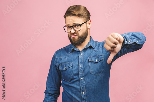 Stylish fashionable male poses indoors against pink background, assess project, shows sign of dislike, looks with negative expression and disapproval. Disagreement, disgust and negative expressions