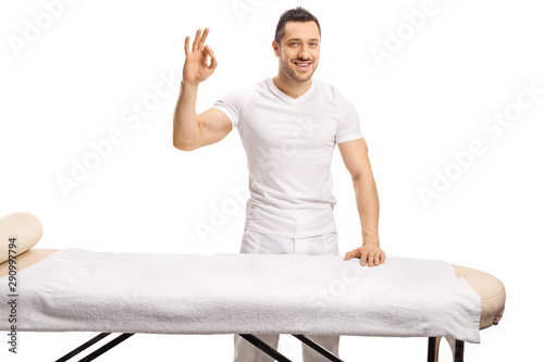 Professional young masseur standing behind a massage bed and gesturing sign good photo