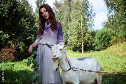 Fashion beauty portrait of young brunette woman with goats walk in a forest park. Conteptual scenic photo in a summer time photo