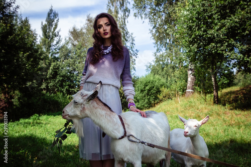 Fashion beauty portrait of young brunette woman with goats walk in a forest park. Conteptual scenic photo in a summer time photo