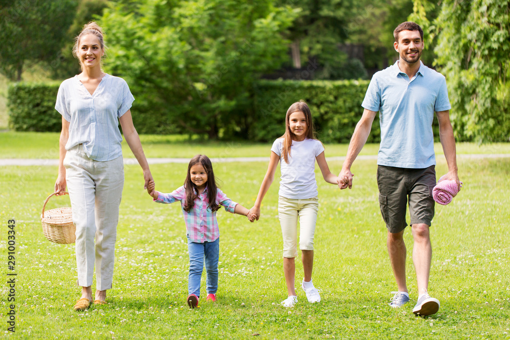 family, leisure and people concept - happy mother with picnic basket, father and two daughters walking in summer park