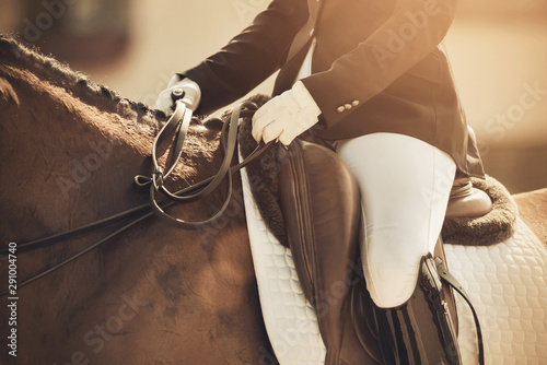 A rider riding a horse, holding his reins, participating in dressage competitions on a Sunny day.