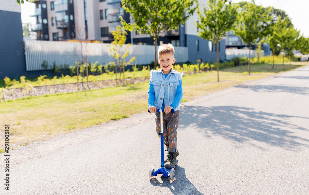 Obraz premium childhood, leisure and fun concept - happy little boy riding scooter in city