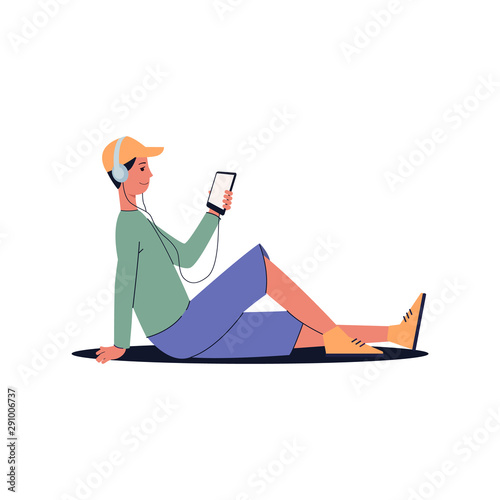 Man sitting on the floor with headphones listening to music, looking at phone