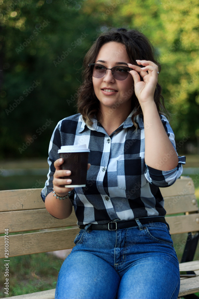 girl drinks coffee from a disposable cup in the park on a bench