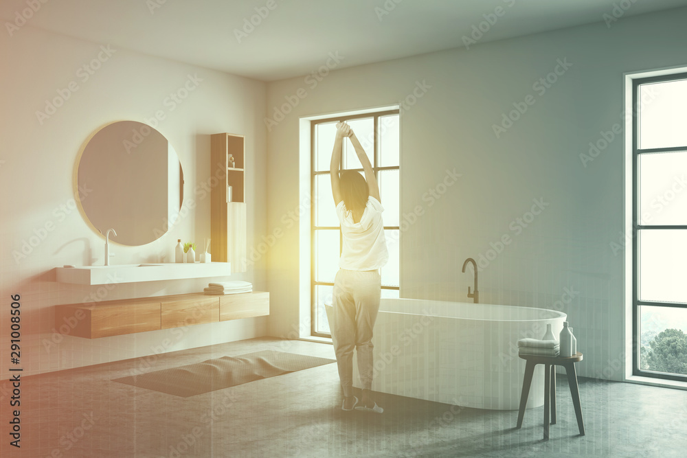 Woman in white bathroom with sink and tub