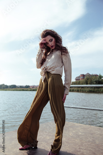 Young fashionable woman in stylish clothes posing near river side in a summer evening. Fashion model