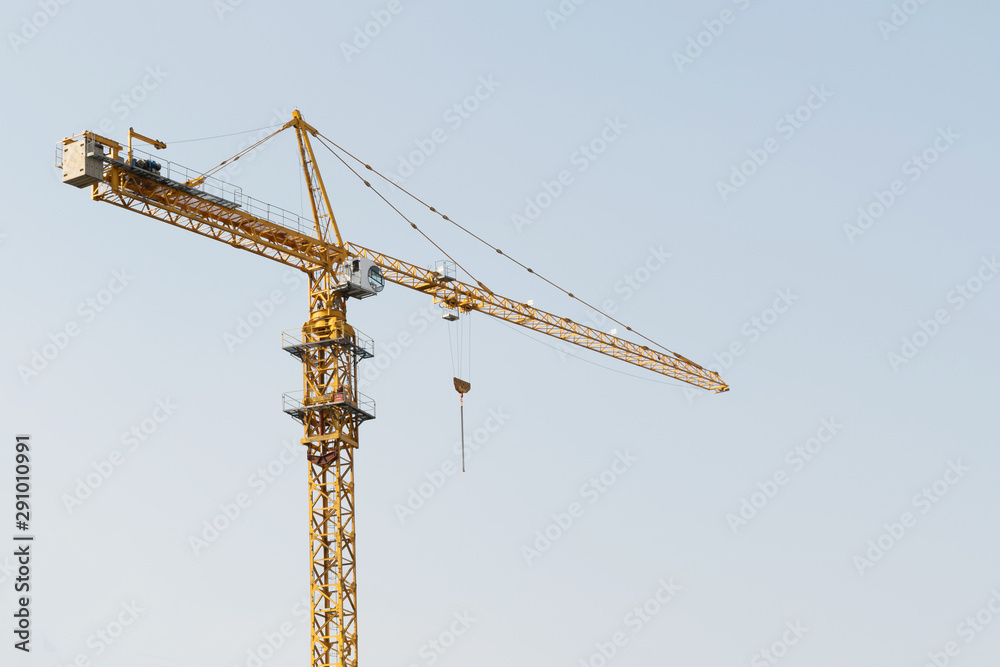 A yellow high-rise building crane against a blue sky builds multi-storey apartment buildings using modern technologies of metal, concrete and brick according to an architectural project A yellow high-rise building crane against a blue sky builds multi-storey apartment buildings using modern technologies of metal, concrete and brick according to an architectural project