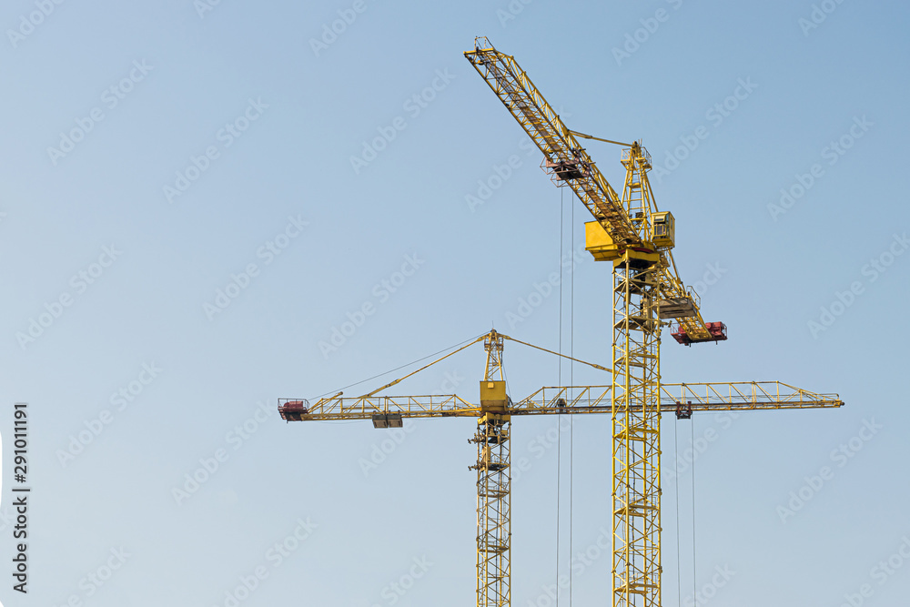 A yellow high-rise building crane against a blue sky builds multi-storey apartment buildings using modern technologies of metal, concrete and brick according to an architectural project A yellow high-rise building crane against a blue sky builds multi-storey apartment buildings using modern technologies of metal, concrete and brick according to an architectural project