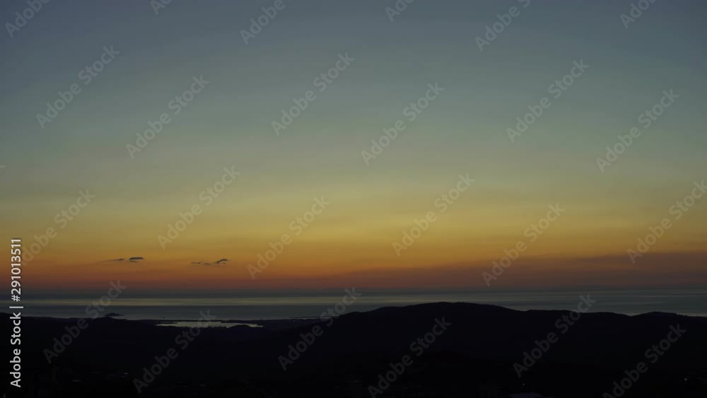Amazing shot of sunrise over the sea. Sun rising up at morning over the sea and sky getting brighter and blue on the city of Arbatax, Sardinia isle, Italy. Time lapse. Cine lens.