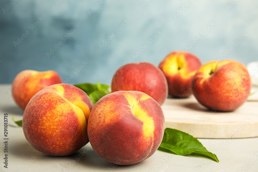 Tasty fresh peaches with leaves on grey table against blue background Tasty fresh peaches with leaves on grey table against blue background