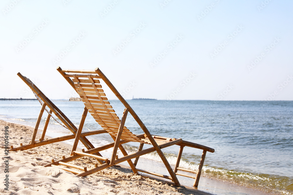 Sandy beach with empty wooden sunbeds on sunny day Sandy beach with empty wooden sunbeds on sunny day