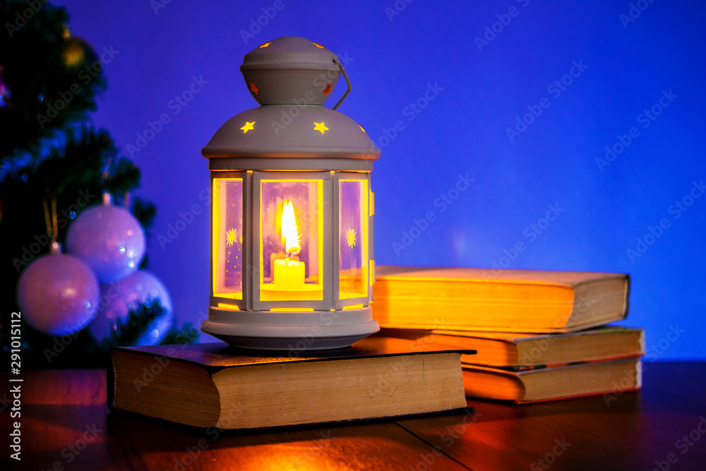 Lantern with candle and books near the Christmas tree_ Lantern with candle and books near the Christmas tree_